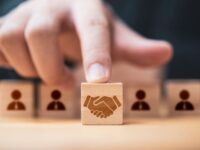Hand putting hand shaking which print screen on wooden cube block  in front of human icon for business deal and agreement concept.
