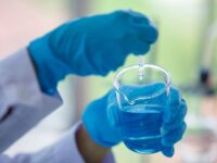 Close up hand laboratory beaker with blue liqid in analyst's hand in plastic glove blur background. Concept Science experiment